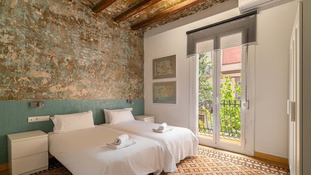 A bedroom with two beds, a balcony, and a rustic wall. - Stay U-nique Apartments Nació (Barcelona)
