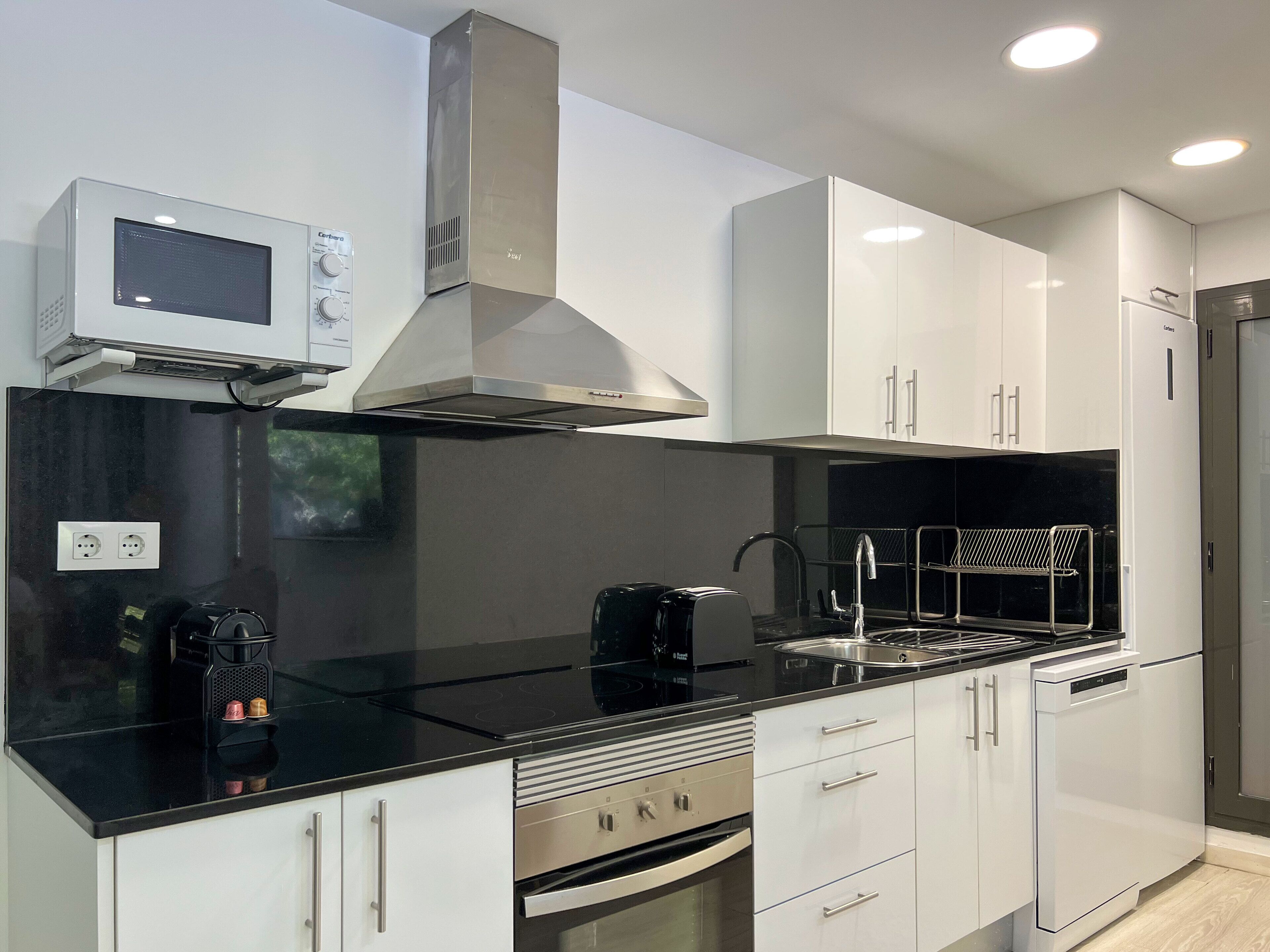 Een moderne keuken met witte kastjes, een zwart aanrecht, roestvrijstalen apparatuur en een inbouwmagnetron.