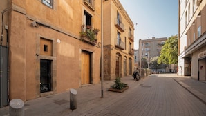 Una tranquilla strada cittadina con edifici dall'architettura tradizionale, caratterizzati da porte in legno e balconi fioriti.