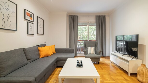 Uma sala de estar moderna com um sofá cinzento, uma mesa de centro branca e uma TV em um suporte.