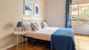 Quarto com cama, mesa de cabeceira, luminária e duas fotos emolduradas na parede.
