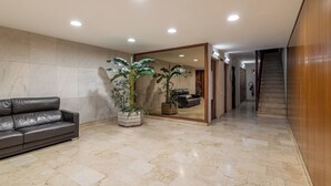 Um hall moderno com um sofá de couro, plantas em vasos grandes, uma parede espelhada e uma escada.