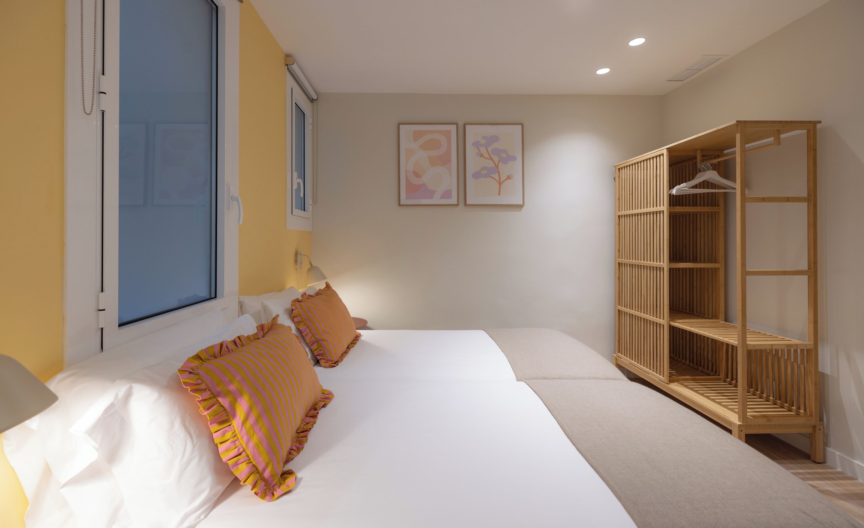 Een slaapkamer met een bed, kussens, een kledingkast en twee ingelijste foto’s aan de muur.