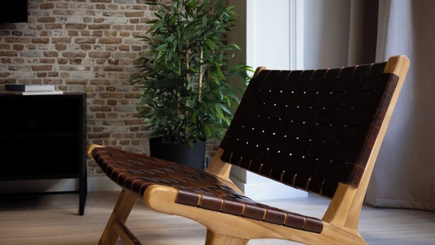 A wooden chair with a woven backrest and seat, positioned in a room with a brick wall, a potted plant, and a black cabinet. - Stay U-nique Apartment Muntaner (Barcelona)