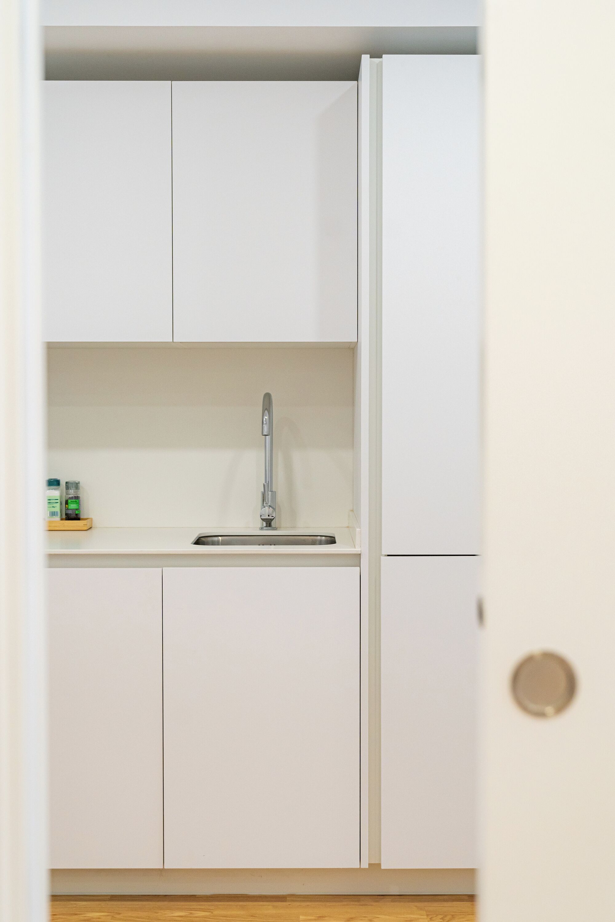 A kitchen with white cabinets, a stainless steel sink, and a wooden floor.