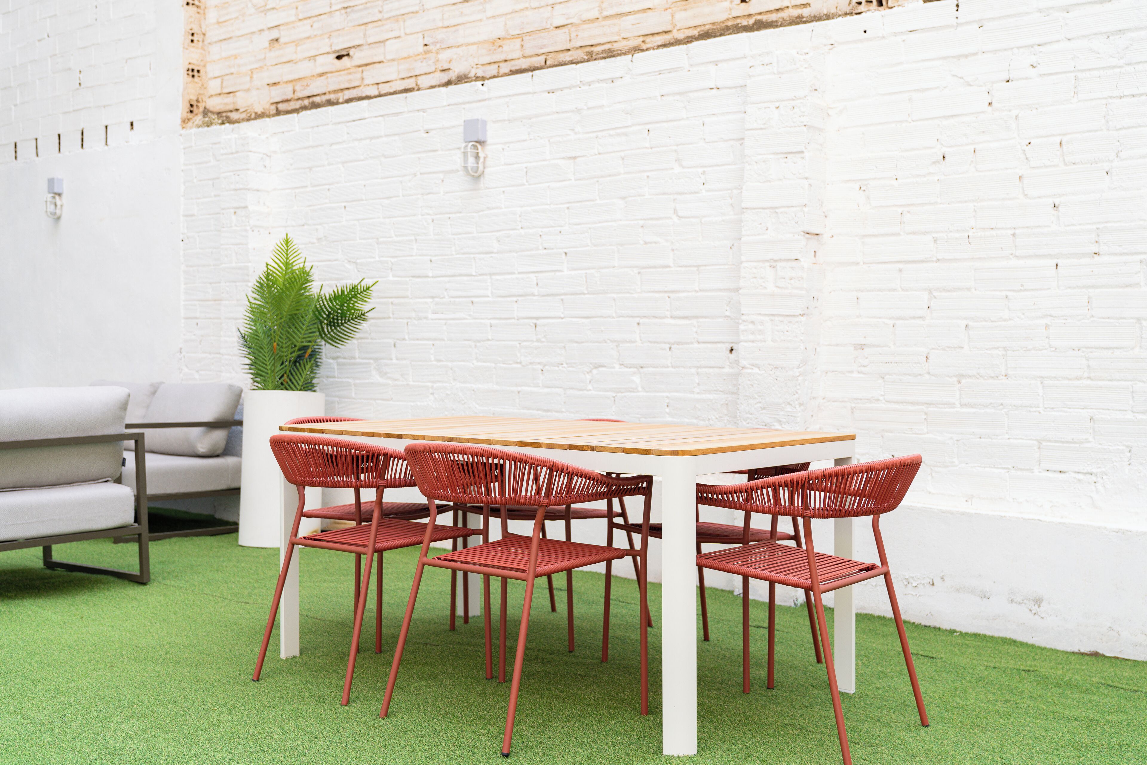 A dining area with a white brick wall, a wooden table, and red chairs.