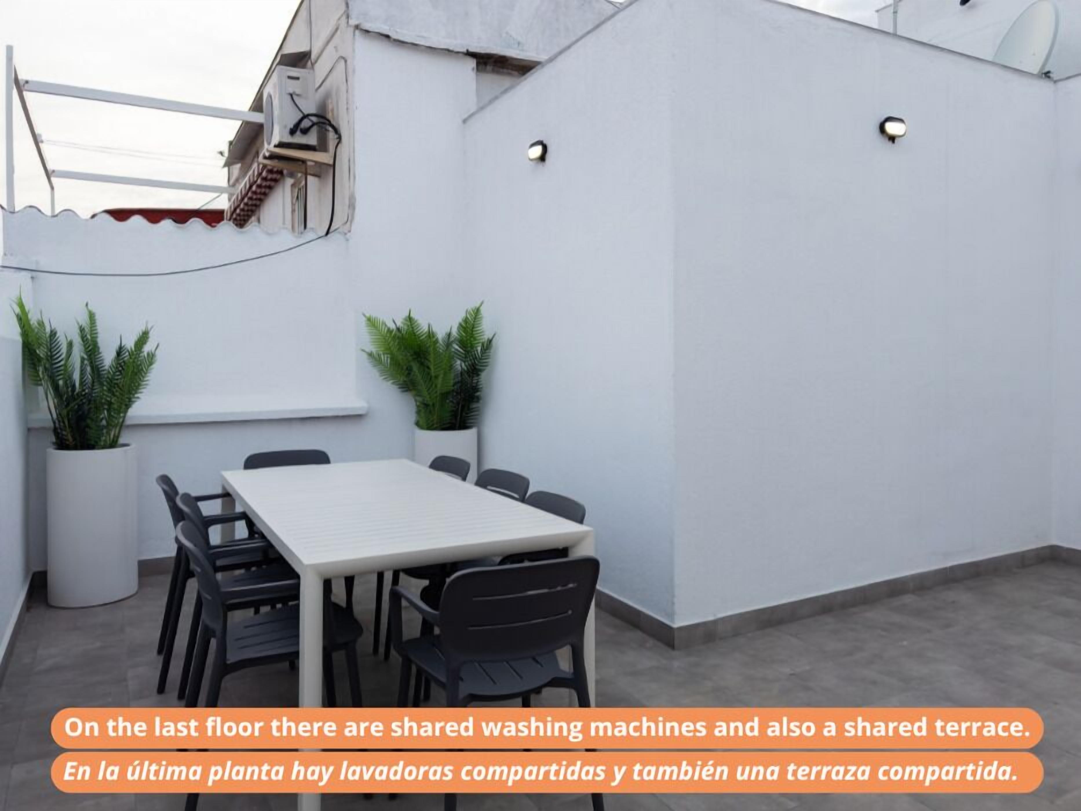 A rooftop terrace with a table and chairs, potted plants, and a satellite dish.