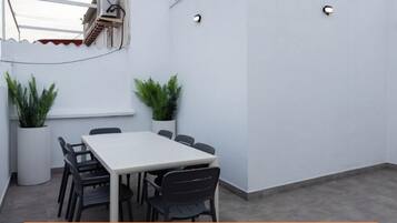 A rooftop terrace with a table and chairs, potted plants, and a satellite dish.