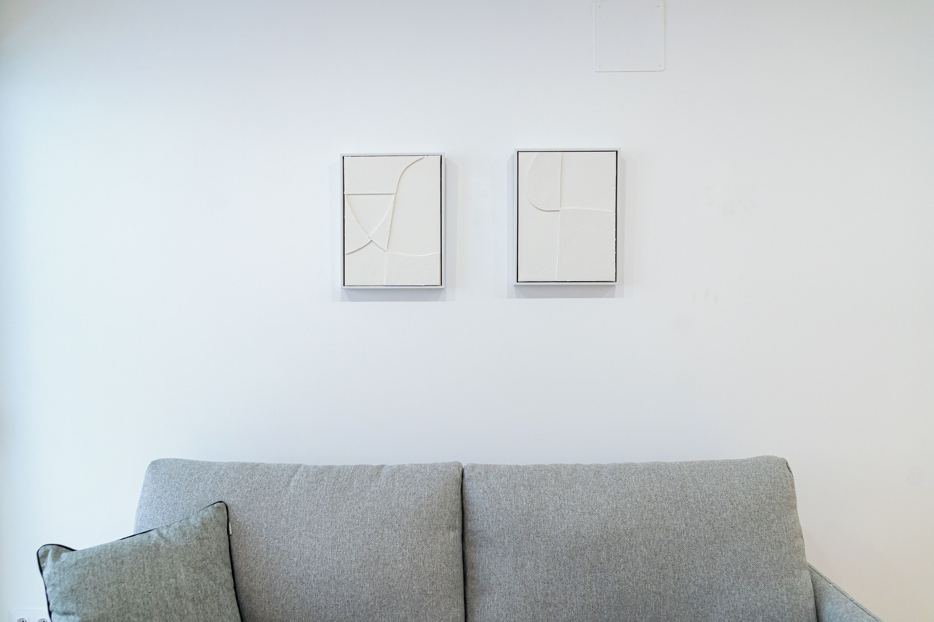 Un salón minimalista con un sofá gris y dos obras de arte abstracto en la pared.