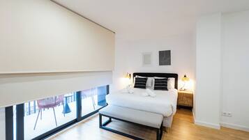 Un dormitorio moderno con un ventanal grande, una cama con reposabajera, lámparas de noche y vistas al exterior.