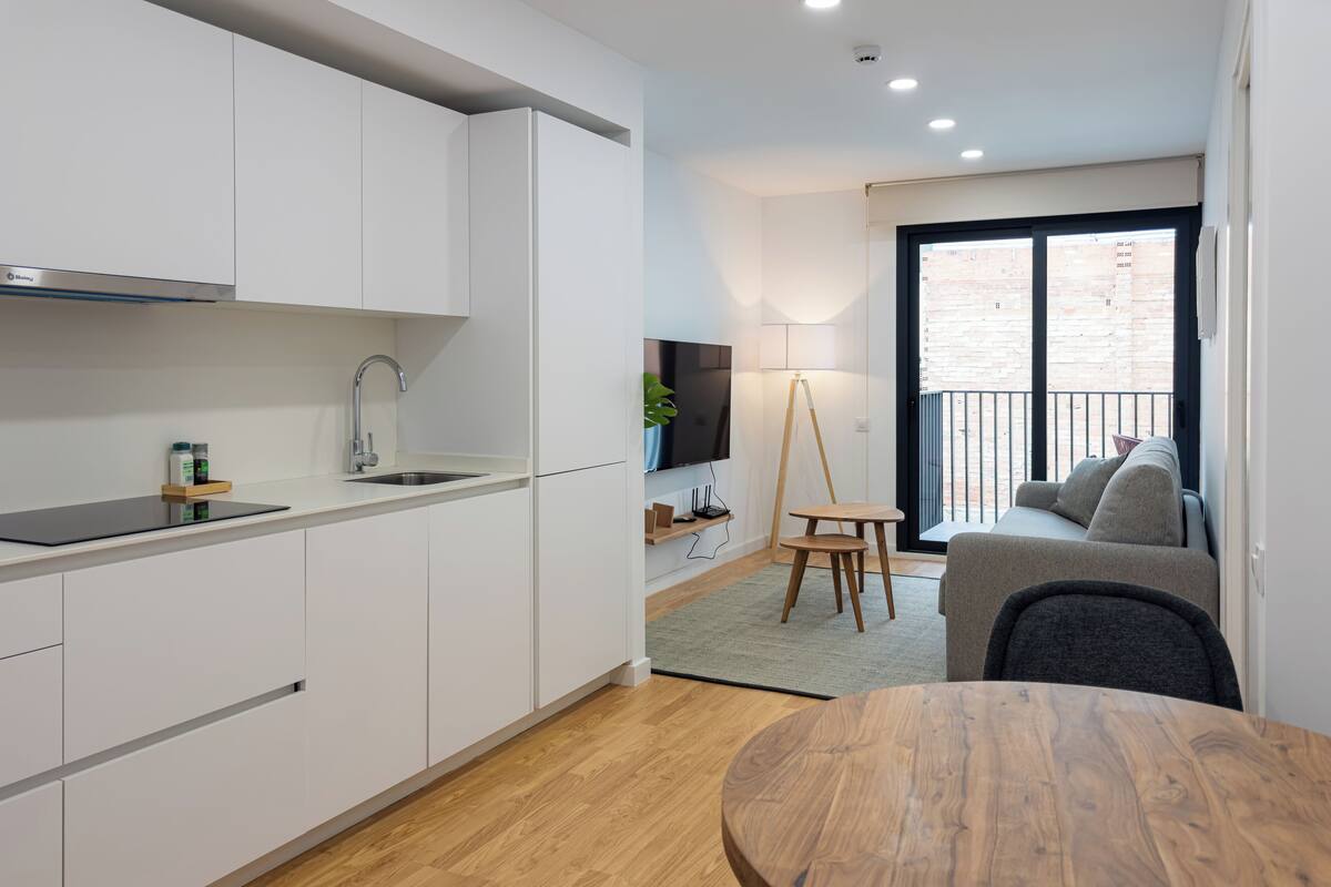 A modern kitchen with white cabinets, a wooden dining table, and a balcony with a sofa.