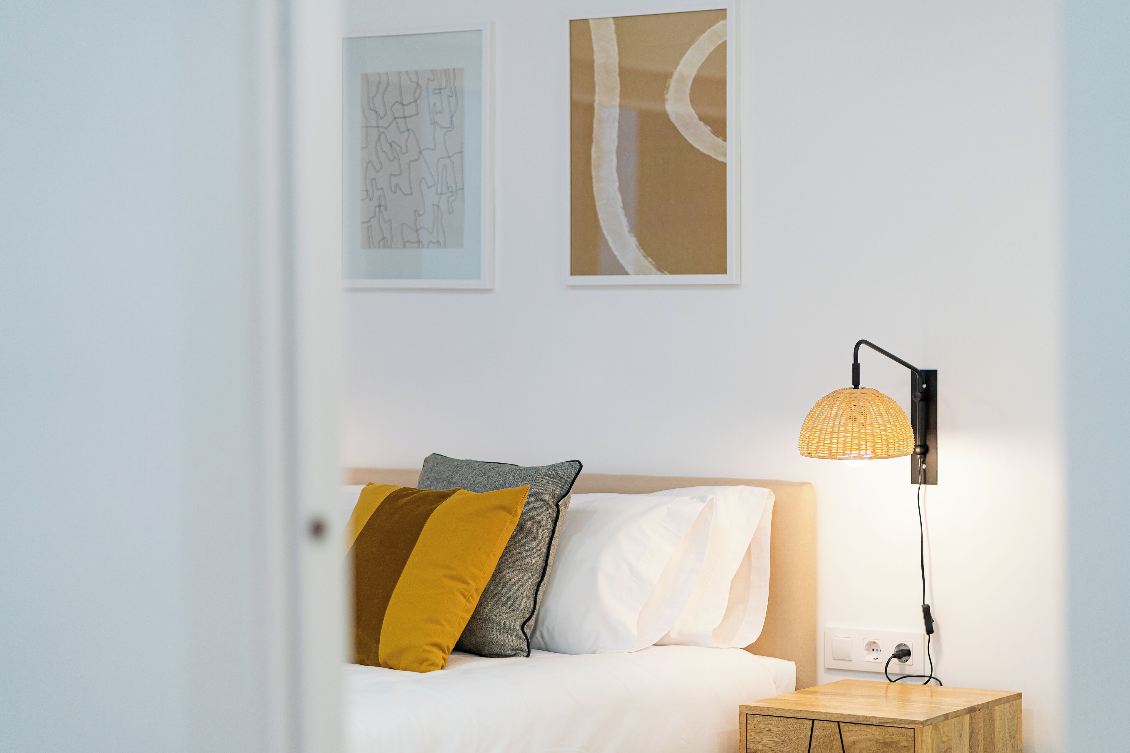 Un lit bien fait, avec des oreillers, une lampe de chevet et deux œuvres d’art encadrées accrochées au mur.
