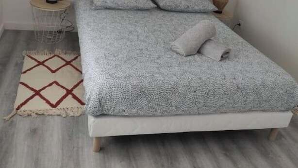 Een slaapkamer met een bed, een klein nachtkastje, een lamp, een vloerkleed en een decoratie aan de muur.