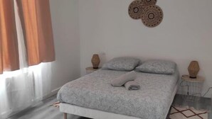 Een slaapkamer met een bed, gordijnen, een wanddecoratie en een nachtkastje.