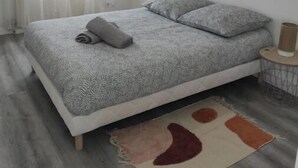 Een slaapkamer met een bed, nachtkastje, gordijnen voor het raam en twee schilderijen aan de muur.