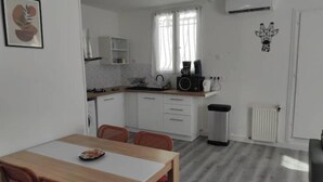 Een kleine keuken met witte kastjes, een eettafel met stoelen, een koffiezetapparaat en een radiator.