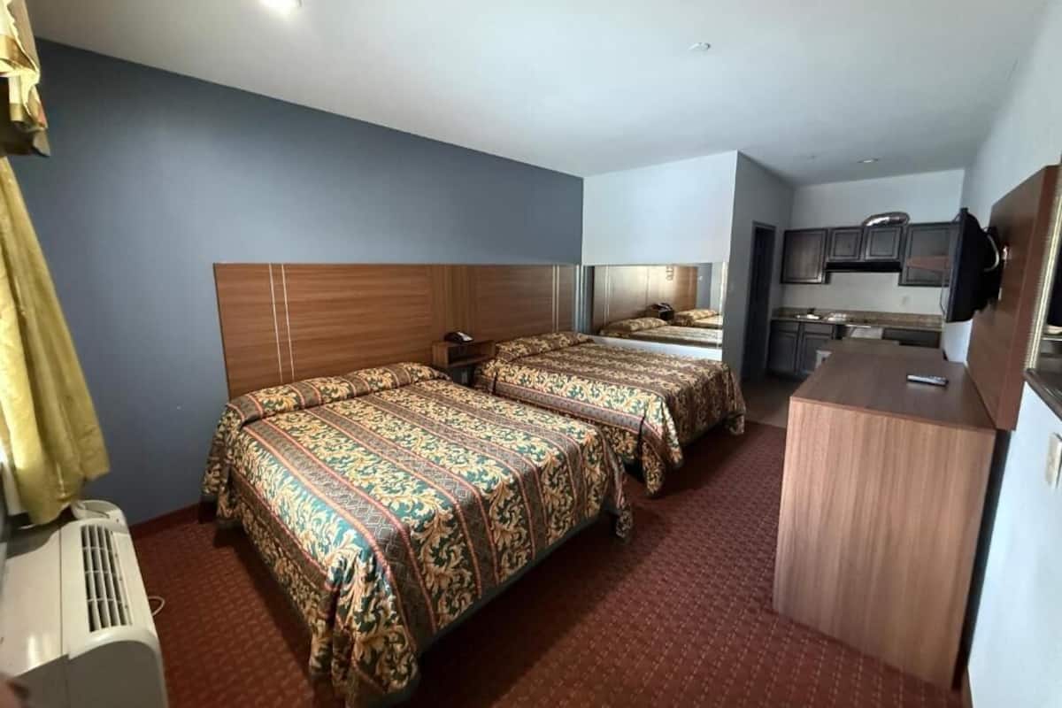 A hotel room with three beds, a kitchenette, and a ceiling fan.