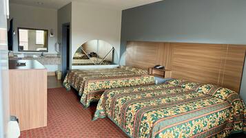 A hotel room with two beds, a wooden headboard, a mirror, a small bedside table, and a desk with a chair.