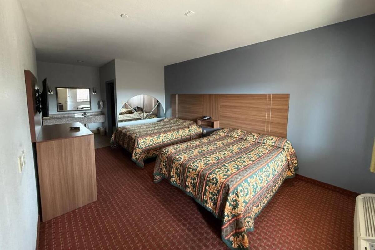 A hotel room with two beds, a wooden headboard, a desk, and a mirror.