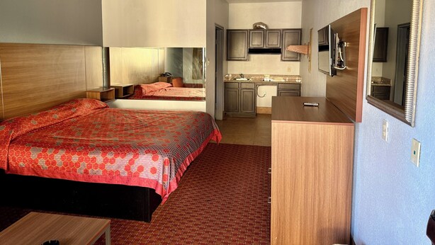 A hotel room with a large bed, a desk, a mirror, and a kitchenette. - Budget Host Inn Stafford - Houston (Houston)