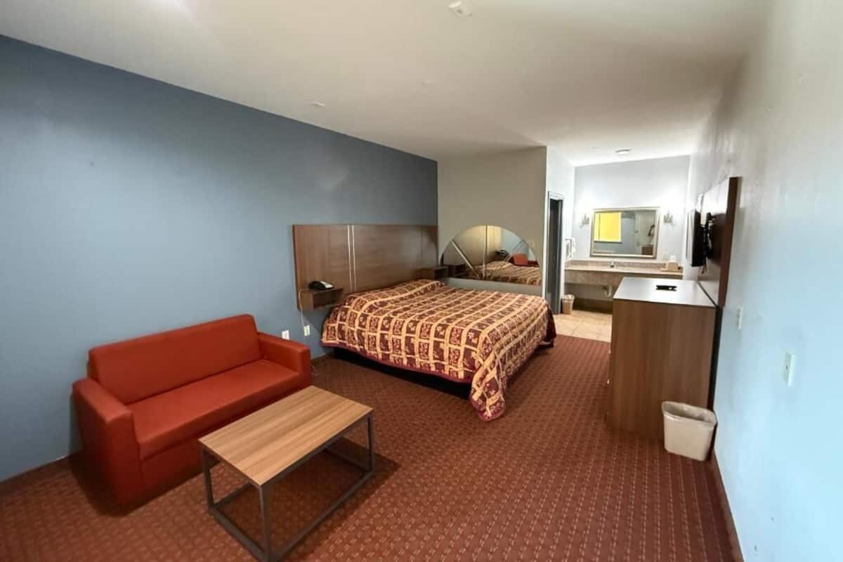 A hotel room with a bed, a red sofa, a wooden table, a desk, and a mirror.