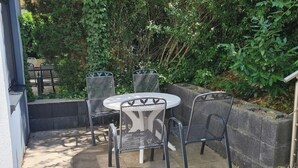 Eine Terrassengruppe im Freien mit einem runden Tisch und vier Stühlen, umgeben von Grünpflanzen und einer Steinmauer.