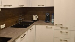 Eine moderne Küche mit weißen Schränken, einer schwarzen Spüle, einem Wasserkocher und einer Kaffeemaschine.