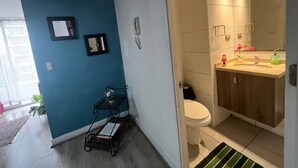 A bathroom with a toilet, sink, and mirror. There is a blue wall and a small table with a plant.
