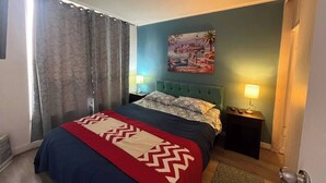 A bedroom with a bed, two bedside lamps, a painting on the wall, and a ceiling fan.