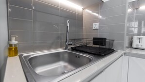 Une cuisine moderne dotée d’un évier en acier inoxydable, d’un égouttoir noir et d’un plan de travail blanc.