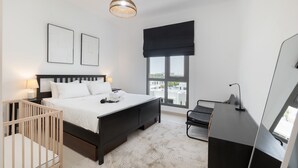 Une chambre moderne avec un grand lit, un bureau, un berceau et une fenêtre donnant sur un beau paysage.