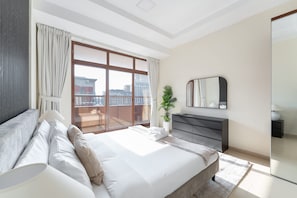 A modern hotel room with a large bed, a dresser, a mirror, and a balcony with a city view. - JVC Apartments Sleeps 5 in Great Location (Dubai)