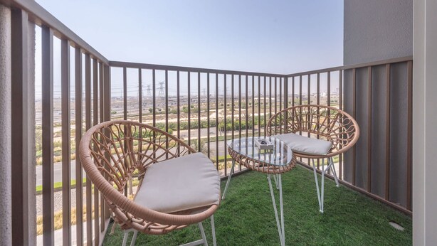 A balcony with wicker chairs and a glass table, overlooking a flat landscape with distant power lines. - Dubai Hills Stunning 1 bed for 4 People (Dubai)