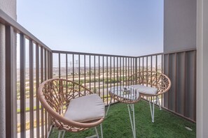Un balcón con sillas de mimbre y una mesa de vidrio, con vistas a un paisaje llano y líneas eléctricas a lo lejos.