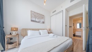 A neatly arranged bedroom with a large bed, a bedside table with a lamp, a wall-mounted painting, and a wardrobe. - Dubai Hills Stunning 1 bed for 4 People (Dubai)