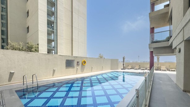 Ein Pool auf dem Dach mit einem blau-weißen Fliesenmuster, umgeben von einer niedrigen Betonmauer und einem Glasgeländer.