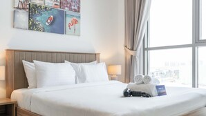 Ein Hotelzimmer mit Bett, Kissen, Nachttisch, Lampe, einem Fenster mit Vorhängen und Blick auf die Stadt.