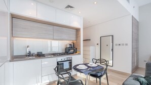 A modern kitchen with white cabinets, a built-in oven, and a dining area with a table and chairs. - Dubai Marina Studio for 2 With Sea Views (Dubai)