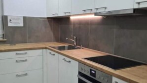 Een moderne keuken met witte kastjes, een houten aanrechtblad, een inbouwoven en een roestvrijstalen spoelbak.