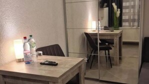 Een kleine kamer met een houten tafel en stoelen, een spiegel en een raam met uitzicht op een gebouw.