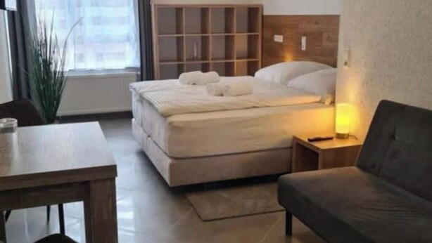 Een slaapkamer met een bed, nachtkastje, lamp en uitzicht op de stad.