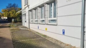 Een gebouw met een witte gevel, nummer 36, met een rij ramen en een verhard gebied met een parkeerbord.