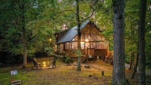 Een chalet in een bos met een houten gevel, een terras en een klein buiten zitgedeelte met verlichting.