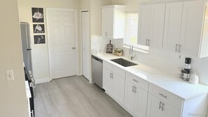 A modern kitchen with white cabinetry, a dishwasher, a sink, and a window with blinds.