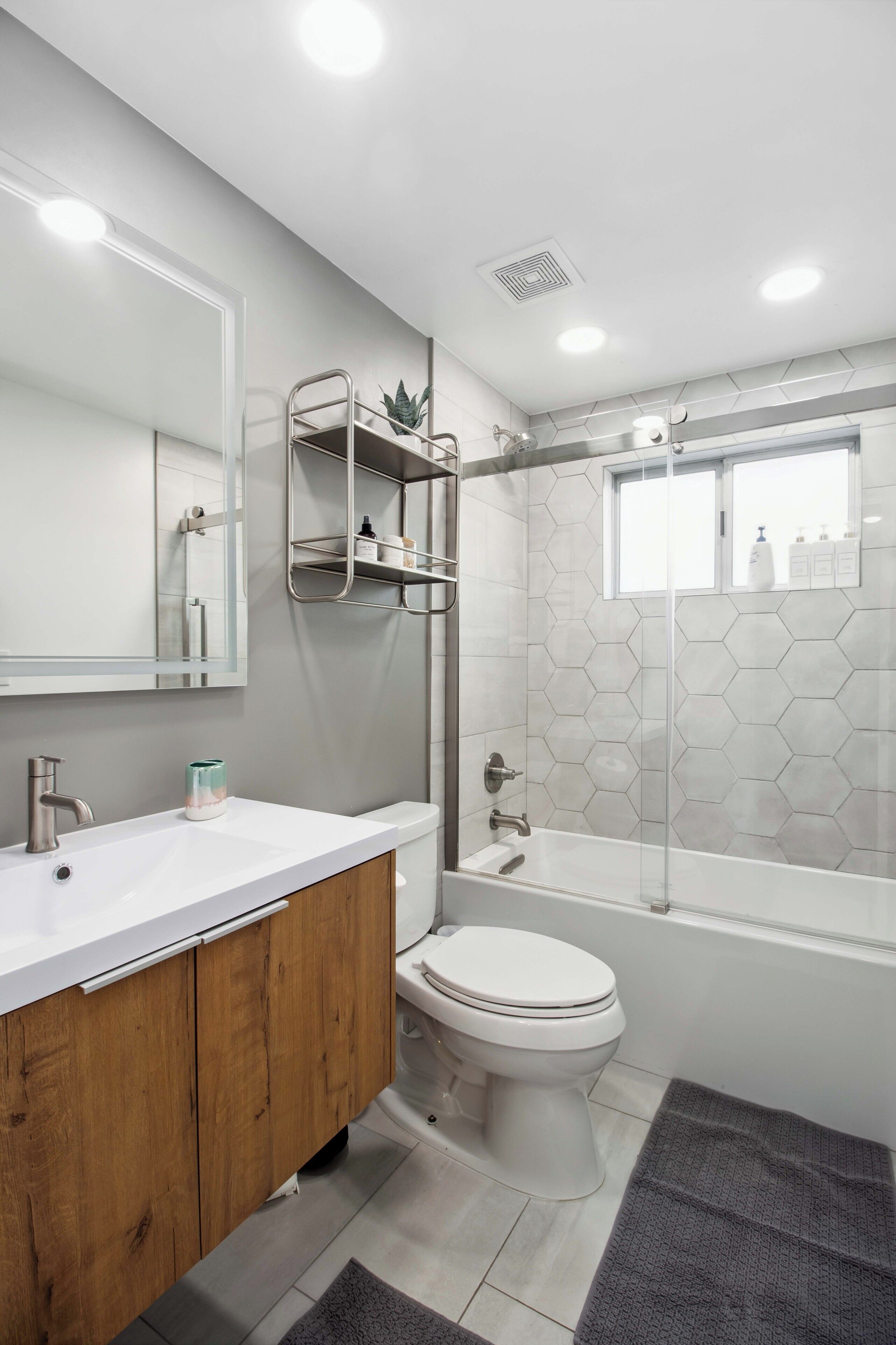 A modern bathroom with a white sink, wooden vanity, a white toilet, and a glass-enclosed shower area.