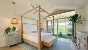Une chambre spacieuse avec un lit à baldaquin, une grande fenêtre donnant sur un paysage verdoyant et un balcon agrémenté d’un fauteuil suspendu.