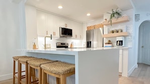 Een moderne keuken met witte kasten, een centraal eiland met barkrukken, een ingebouwde oven en een magnetron.