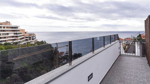 A balcony with a view of the sea and a construction crane in the background.