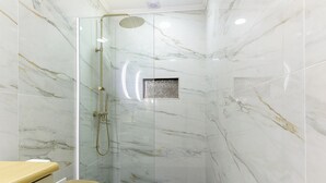 A glass-enclosed shower with a handheld showerhead, a small square window, and a black tiled floor.