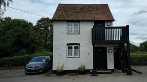 A small, white two-story building with a black balcony and a black door. There are two cars parked in front. - The George & Dragon Pub - The Stable (Horsham)